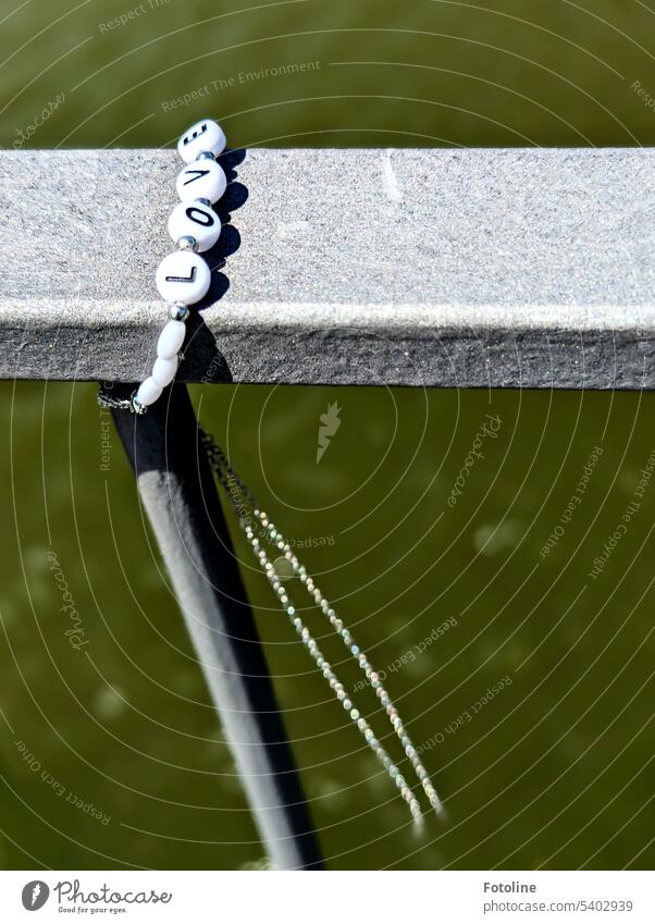 An der Brücke über den Mittellandkanal hat jemand ein Kettchen angebracht, mit Perlen mit der Aufschrift "LOVE" Geländer Metall Stahl Licht grau Wasser Kette