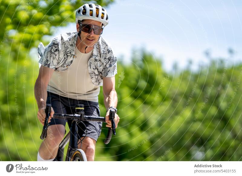 Sportler auf dem Fahrrad auf dem Lande vor unscharfem Hintergrund Radfahrer Mitfahrgelegenheit Schutzhelm Sonnenbrille Park Sommer männlich Athlet aktiv