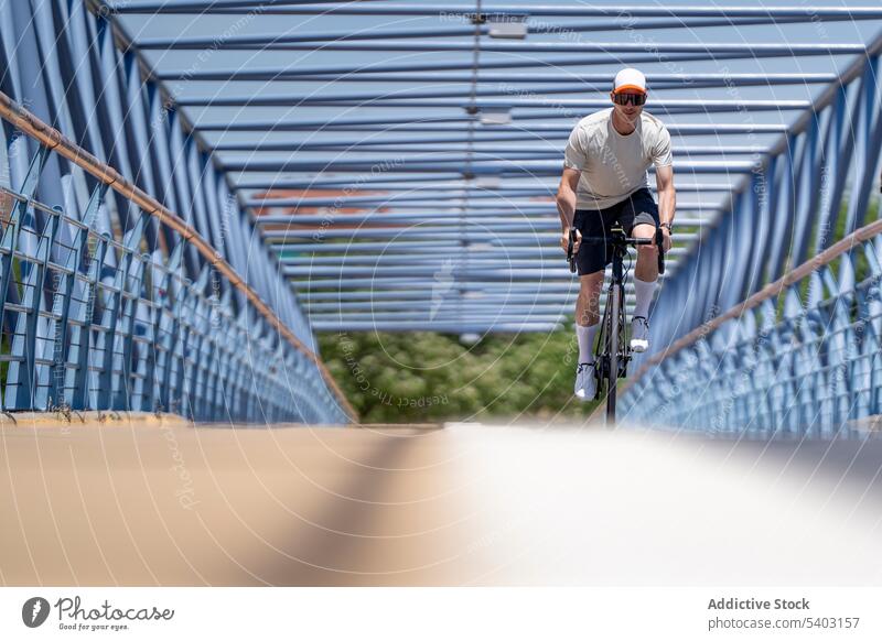Sportler fährt Fahrrad auf der Straße der Brücke im Sommer Radfahrer Mitfahrgelegenheit Hut Sonnenbrille Sportbekleidung männlich Athlet aktiv dynamisch