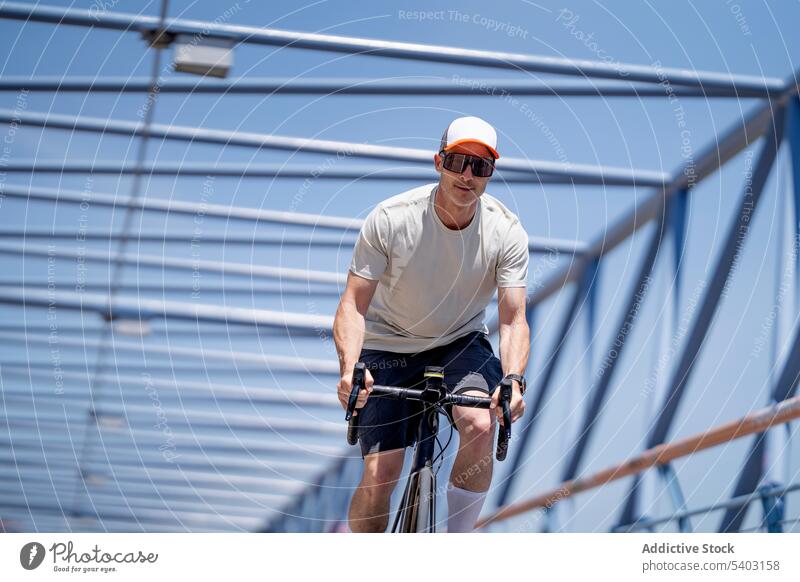 Sportler fährt Fahrrad auf der Straße der Brücke im Sommer Radfahrer Mitfahrgelegenheit Hut Sonnenbrille Sportbekleidung männlich Athlet aktiv dynamisch