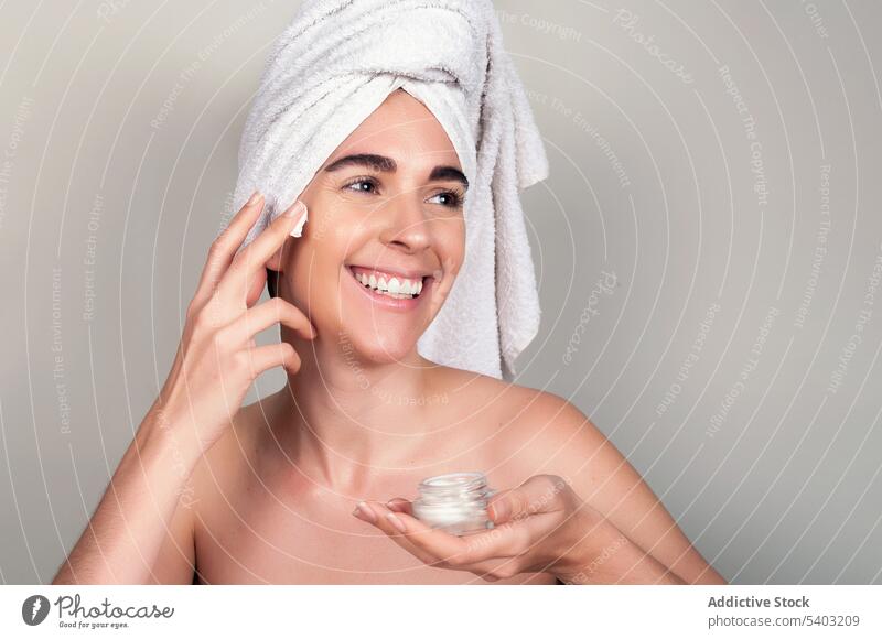 Glückliche Frau mit einem Handtuch um den Kopf, die eine kosmetische Maske und Creme auf das Gesicht aufträgt Hautpflege bewerben Mundschutz Sahne Verfahren