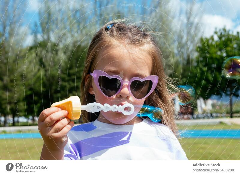 Kleines Mädchen bläst Seifenblasen im Park Schlag Kind spielen Rasen Spielzeug Kindheit bezaubernd wenig grasbewachsen Gras Sonnenbrille niedlich spielerisch