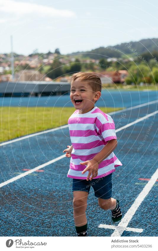 Glücklicher Junge läuft tagsüber auf der Rennstrecke laufen Lächeln heiter Lachen Kind Aktivität Sportpark Spaß Energie bezaubernd spielerisch Kindheit Freude