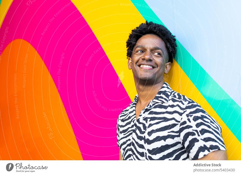 Fröhlicher junger Mann in der Nähe einer bunten Wand positiv Lächeln Porträt Streifen farbenfroh selbstbewusst Glück Stil schwarz Afroamerikaner krause Haare