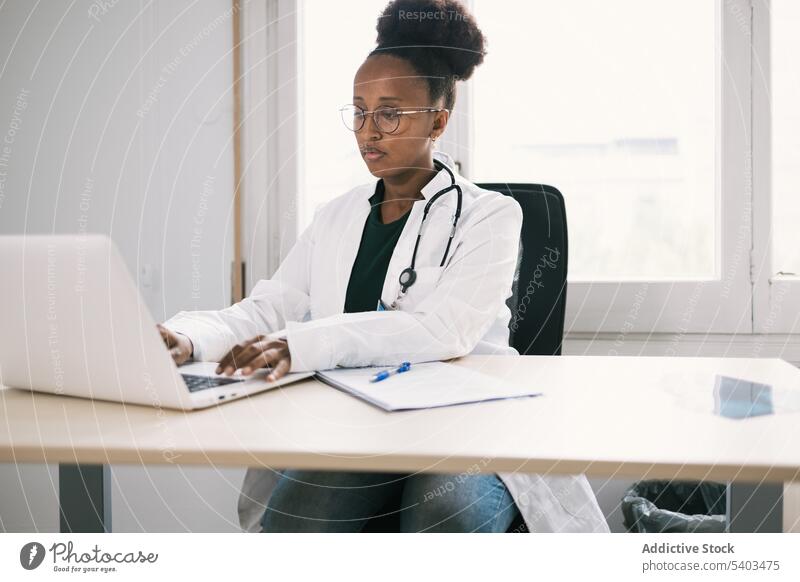 Afroamerikanischer Arzt arbeitet an Laptop Frau arzt Praktiker Gesundheitswesen Tisch Tippen Medizin benutzend Sanitäter Fenster Uniform Arbeit Dame Afro-Look
