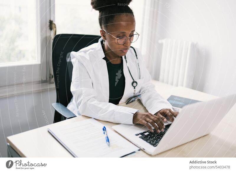 Afroamerikanischer Arzt arbeitet an Laptop Frau arzt Praktiker Gesundheitswesen Tisch Tippen Medizin benutzend Sanitäter Fenster Uniform Arbeit Dame Afro-Look