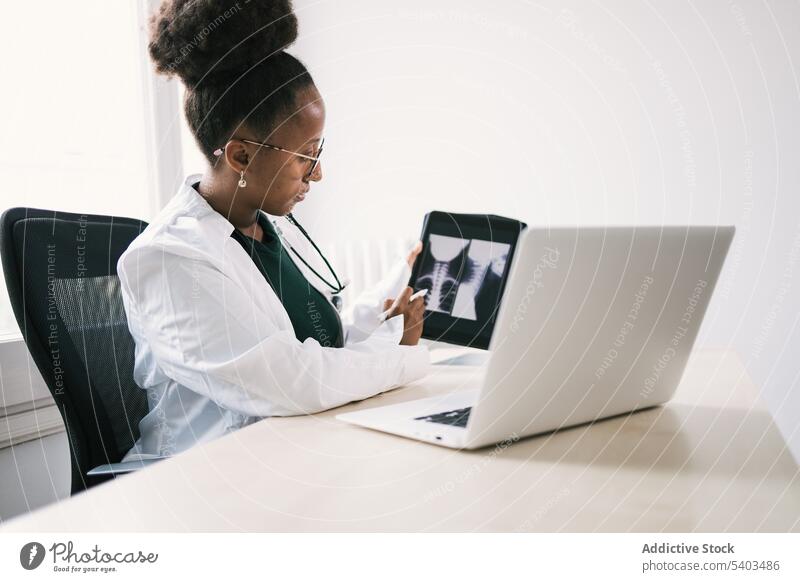 Seitenansicht eines schwarzen Arztes, der am Tisch sitzt und Röntgenbilder auf einem Tablet zeigt Frau Uniform Stethoskop Tablette Spezialist professionell Raum