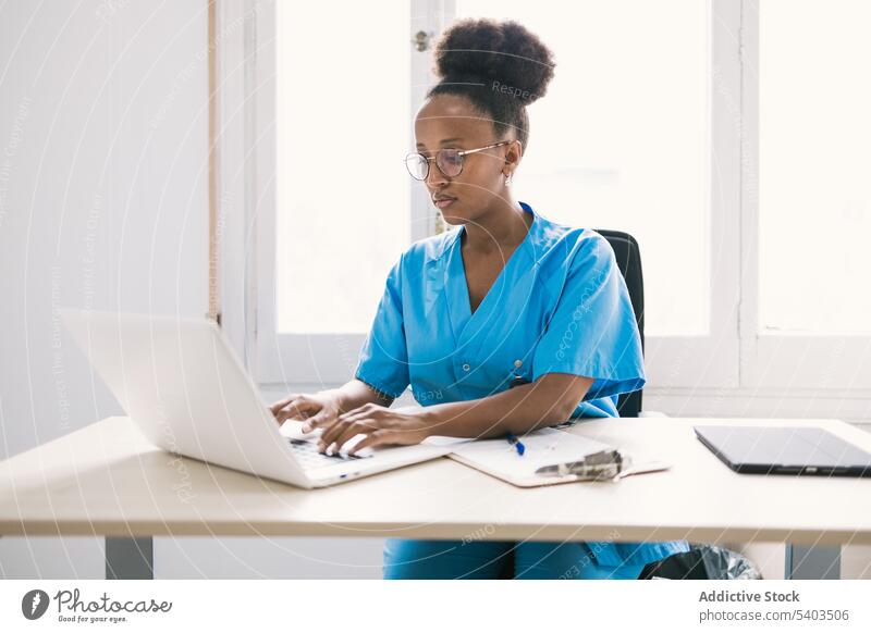 Schwarze Ärztin sitzt und arbeitet am Laptop Frau Arzt Konzentration online Arbeit Fokus Uniform professionell Arbeitsplatz jung ethnisch Afroamerikaner schwarz