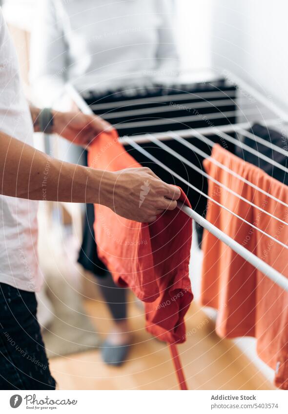 Crop Mann in Freizeitkleidung hängen saubere Kleidung in der Nähe Ernte Frau im Zimmer zu Hause Erwachsener Sauberkeit übersichtlich Bekleidung häusliches Leben