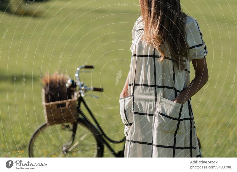 Gesichtslose Frau mit Fahrrad auf grasbewachsenem Feld Blume Korb Natur Gras Kleid lange Haare friedlich jung Sommer Landschaft geblümt Lifestyle idyllisch Dame