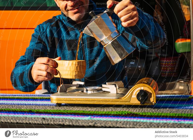 Ein glücklicher Tourist, der Kaffee aus einer Moka-Kanne einschenkt Mann Moka-Topf Kleintransporter Wohnmobil eingießen trinken Glück Lächeln Campingplatz