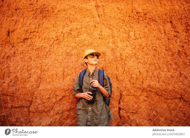 Stylischer Jugendlicher mit Sonnenbrille und Wasserflasche am Sandstein stehend Teenager Junge besinnlich Tourist Reisender nachdenklich Kalkstein Tourismus