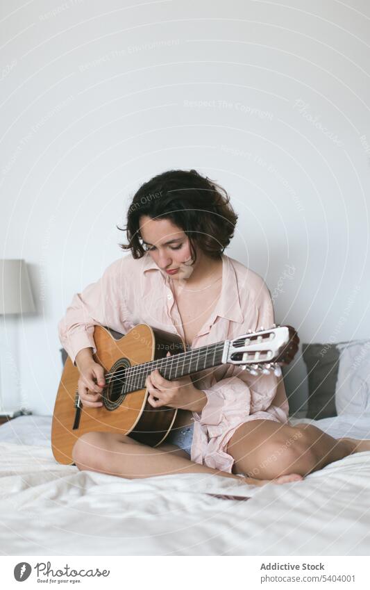 Seriöse junge Frau spielt Gitarre auf dem Bett im Schlafzimmer spielen Musik üben akustisch Hobby Freizeit sich[Akk] entspannen heimwärts Instrument