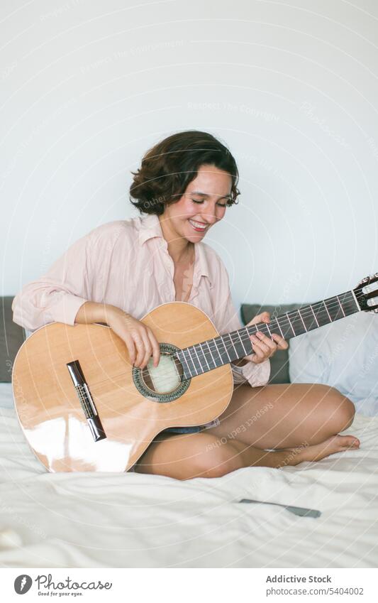 Zufriedene junge Frau mit geschlossenen Augen spielt Gitarre auf dem Bett im Schlafzimmer spielen Musik üben akustisch Hobby Freizeit sich[Akk] entspannen