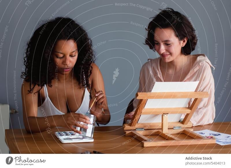 Verschiedene Frauen am Tisch sitzend mit Pinsel und Wasserfarben Freund Farbe mischen Bürste Konzentration Lächeln jung Afroamerikaner schwarz vielfältig