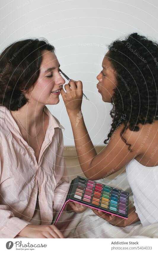 Schwarze Frau trägt Make-up mit Pinsel auf das Auge ihrer Freundin auf Frauen zu Hause bewerben Bürste Lidschatten Lächeln Schönheit positiv jung vielfältig