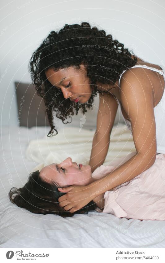 Schwarze Frau sitzt und berührt das Haar ihrer vielfältigen Freundin Frauen Partnerschaft Bonden Bett sanft Angebot berühren Leidenschaft jung