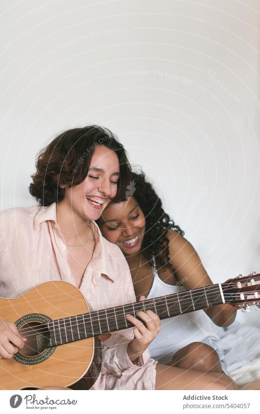 Fröhliches lesbisches Paar spielt Gitarre zu Hause spielen Freundin heiter Freizeit genießen Zusammensein Musik Spaß Bett Frauen heimwärts Glück Kälte