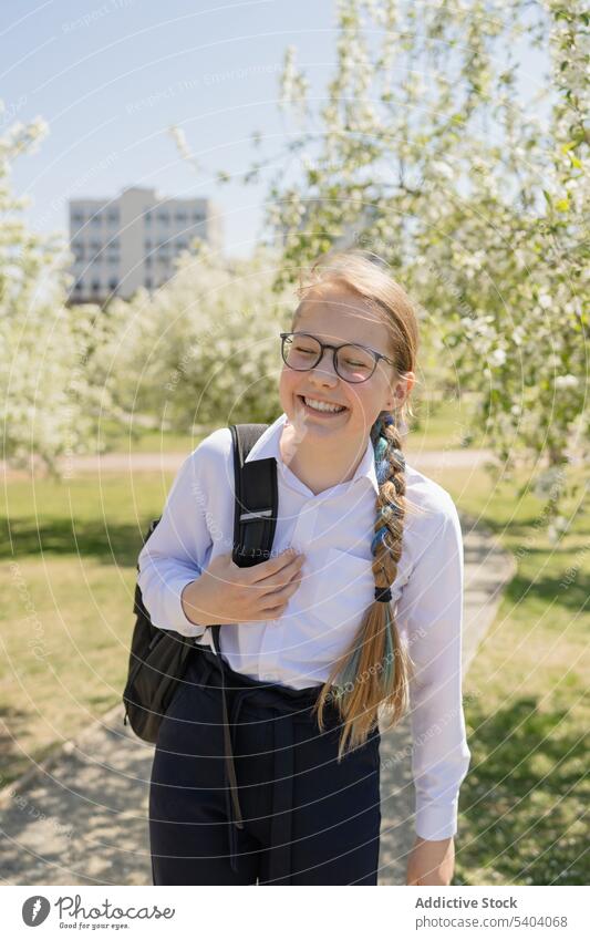 Lächelndes jugendliches Mädchen mit Schultasche im Park stehend Teenager Schulmädchen heiter sorgenfrei Augen geschlossen positiv Jugendlicher Sonnenlicht Glück