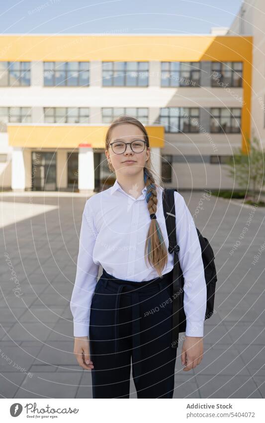 Positives jugendliches Schulmädchen mit Tasche in der Nähe eines Gebäudes stehend Mädchen Schule Teenager Uniform Schüler zurück zur Schule Jugendlicher Pupille