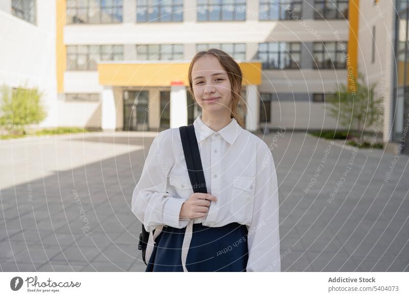 Glückliche Teenager-Schülerin mit Tasche in der Nähe eines Gebäudes Mädchen Schule Lächeln Uniform zurück zur Schule Jugendlicher Pupille Rucksack Schulmädchen