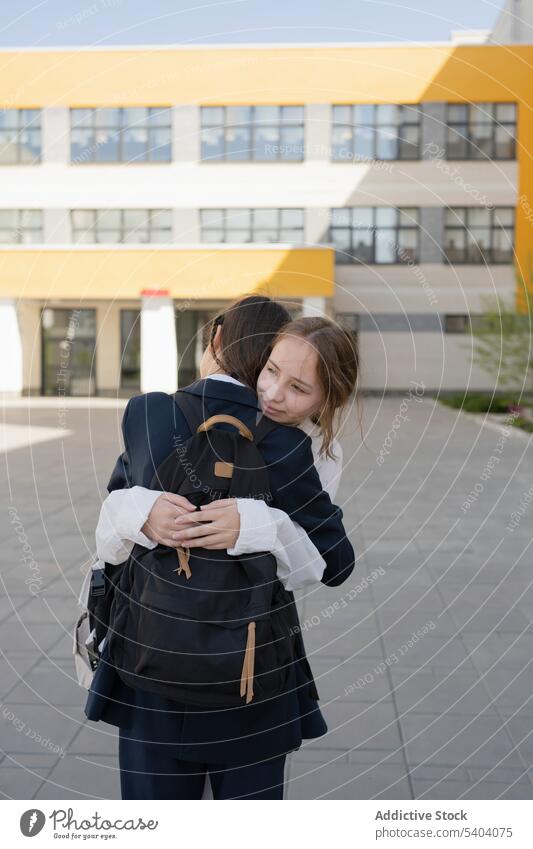 Glückliche Schulmädchen stehen und umarmen sich in der Nähe des Schulgebäudes Schüler Schule Teenager Campus Umarmung Lächeln Klassenkamerad Umarmen