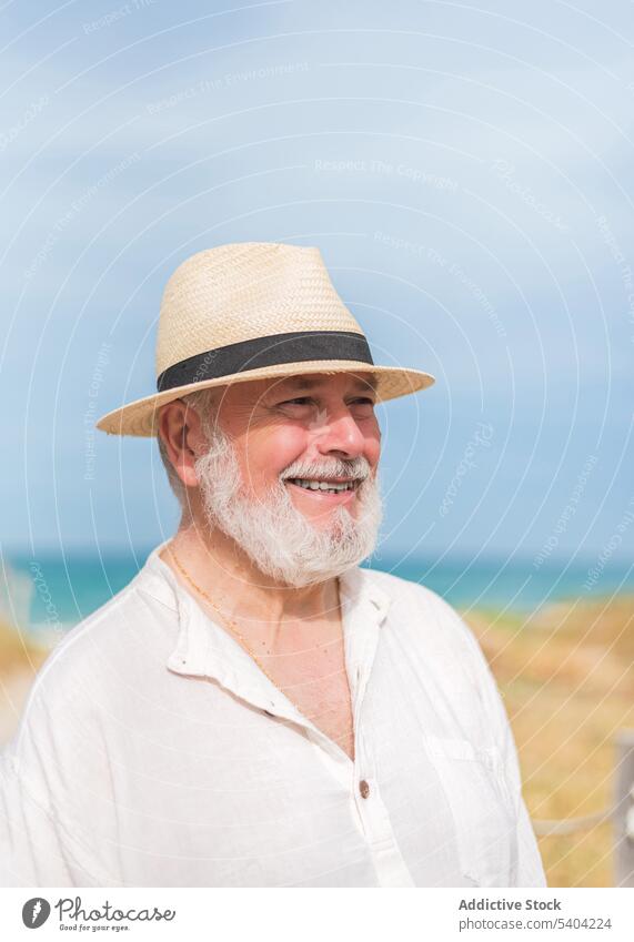 Heiterer älterer Mann mit Hut am Strand stehend Glück Porträt in den Ruhestand gehen Lächeln froh Küste Feiertag heiter Meeresufer Ufer Urlaub Sommer positiv