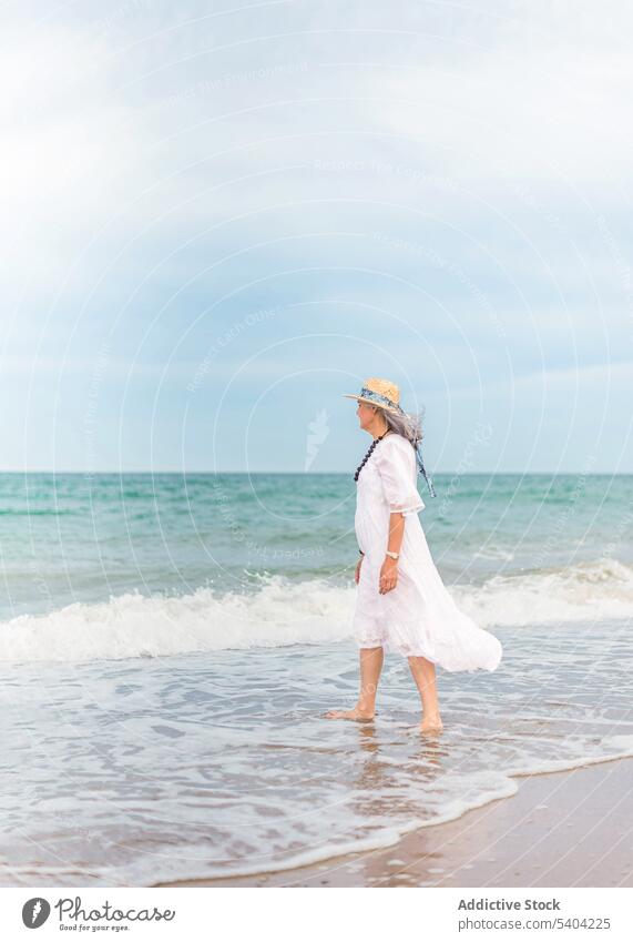 Ernste Frau geht am Sandstrand spazieren Strand Freiheit genießen Urlaub Sommer MEER Natur älter Senior Rentnerin gealtert Ufer winken Wasser Meeresufer Küste