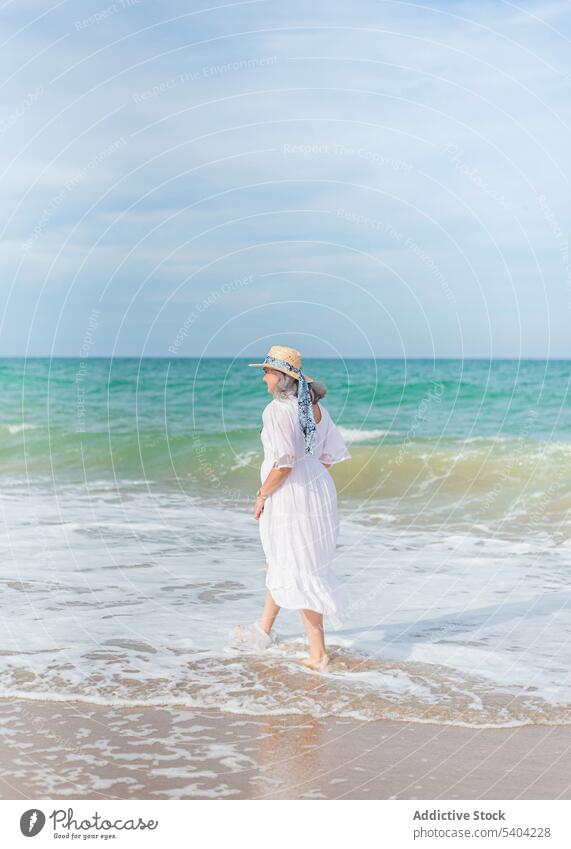 Frau geht am Sandstrand spazieren Strand Freiheit genießen Urlaub Sommer MEER Natur älter Senior Rentnerin gealtert Ufer winken Wasser Meeresufer Küste Strohhut