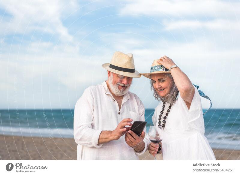 Älteres Paar telefoniert an der Sandküste Smartphone Strand benutzend Resort MEER Wind Browsen Sommer Gerät Apparatur Strohhut Surfen Ufer Partnerschaft