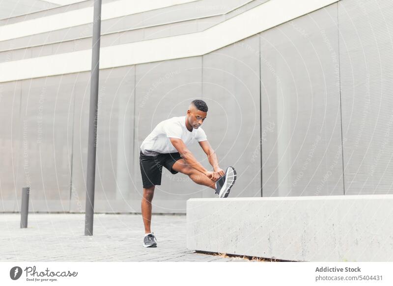 Schwarzer Mann streckt Bein auf Straße Athlet Dehnung Kniesehne Fitness Training Sportbekleidung Turnschuh Großstadt männlich schwarz Afroamerikaner Aufwärmen