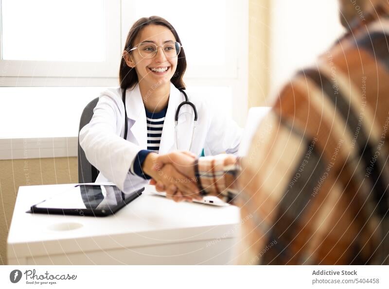 Fröhliche Ärztin begrüßt Patientin im Büro Frau Arzt geduldig Gruß Hände schütteln Lächeln Medizin positiv Gesundheitswesen Spezialist Uniform Ernennung