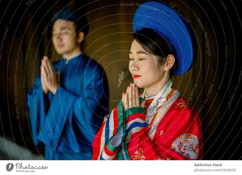 Stilvolles asiatisches Paar in traditioneller Kleidung betet betend Tradition Hut Anbetung Outfit Porträt Hände gefaltet positiv Veranda Zusammensein Hingabe