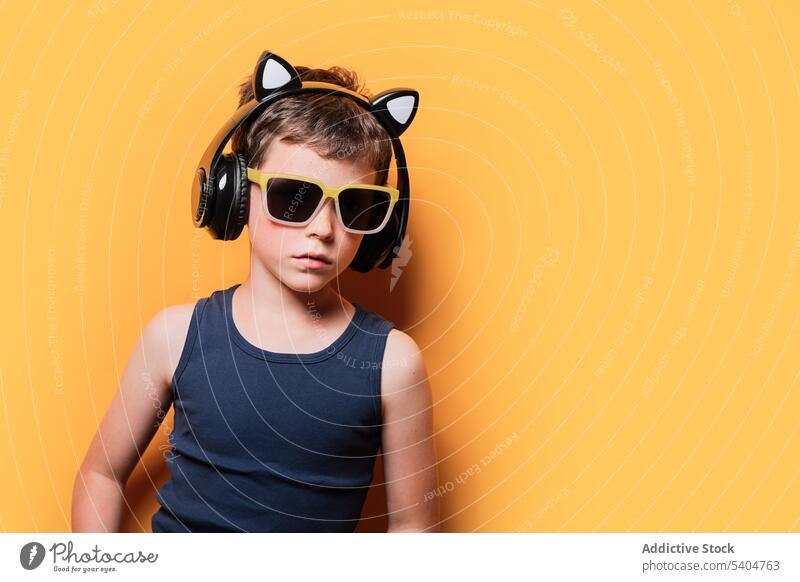 Stylischer Junge mit Sonnenbrille und Kopfhörer auf gelbem Hintergrund trendy zuhören Musik benutzend selbstbewusst Stil Drahtlos Kind Tanktop Shorts Outfit