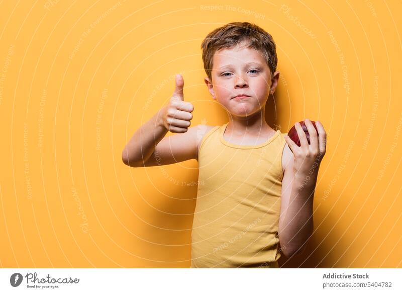 Niedlicher Junge zeigt Daumen hoch und hält Apfel gestikulieren Kind genehmigen Zeichen reif Frucht Porträt Schuljunge zeigen positiv lebhaft lässig