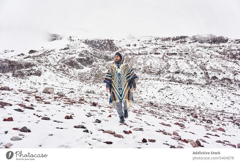 Junger Mann geht auf verschneitem Gelände an einem Berghang Reisender Berge u. Gebirge Fernweh erkunden Natur kalt bewundern Poncho Schnee männlich jung Urlaub