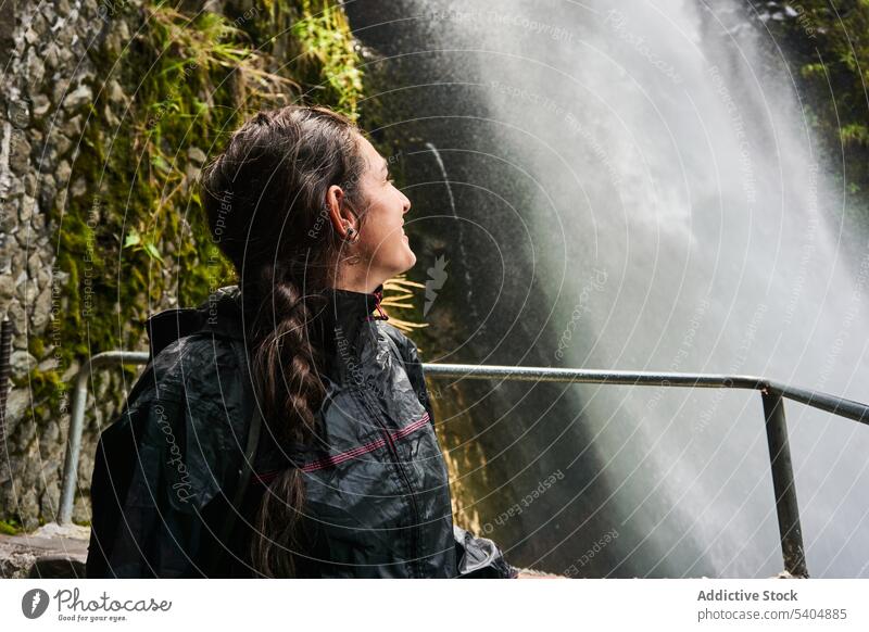 Junge Frau Reisende steht und schaut auf Wasserfall Tourist zuschauen erkunden Rucksack Lächeln Urlaub Reling genießen Abenteuer jung Tourismus Reisender