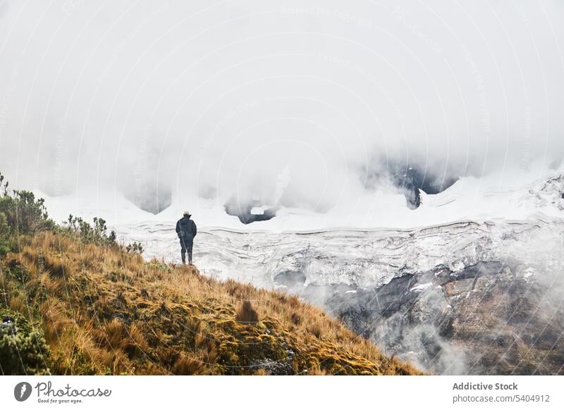 Unbekannter Wanderer auf grasbewachsenem Hang bei bewölktem Berg Berge u. Gebirge Reisender Hügel bewundern Vulkan Natur Top Schnee Landschaft Tal malerisch