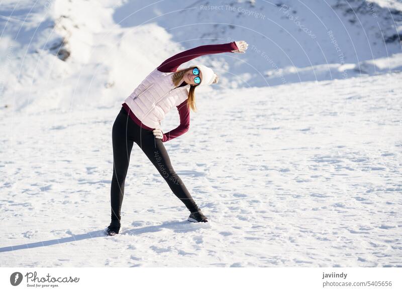 Schlanke Frau in Sportkleidung, die ihren Arm in den verschneiten Bergen zur Seite streckt Dehnung Winter Yoga Übung üben Gesundheit Sportbekleidung Training