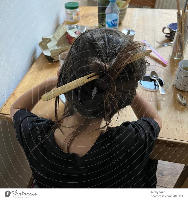 Junge mit langen Haaren trägt Dutt mit Haarnadel aus Bambusholz am Frühstückstisch Tisch lange Haare brünett Haare hochstecken essen frühstücken