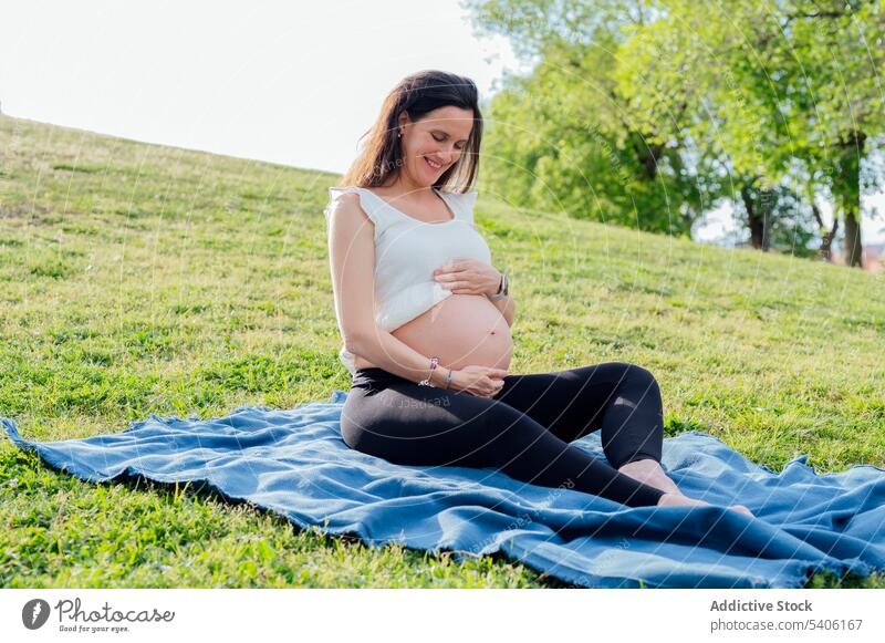 Glückliche schwangere Frau im grünen Park erwarten Bauch mütterlich Gras Straße heiter ruhen Schwangerschaft Kinderkriegen pränatal Mutterschaft vorwegnehmen