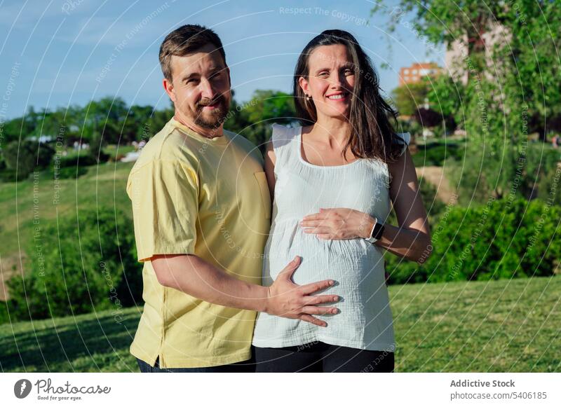 Glückliches Paar in Erwartung umarmt stehend im Park Ehefrau Ehemann schwanger erwarten Bauch mütterlich Umarmen Schwangerschaft Babybauch Kinderkriegen