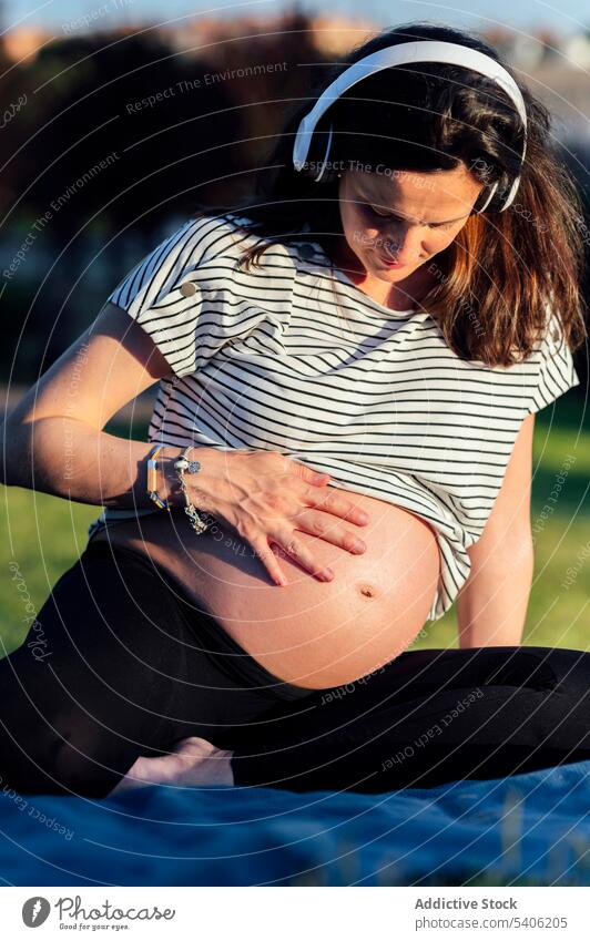 Glückliche schwangere Frau im Gras erwarten Bauch Kopfhörer zuhören Musik Decke Unterlage Kinderkriegen mütterlich pränatal vorwegnehmen Mutter Eltern Mama