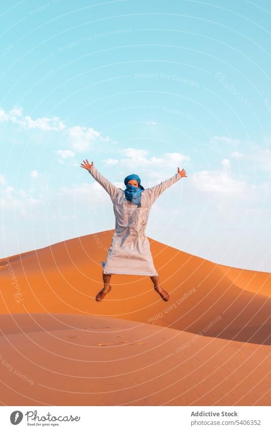 Unbekümmerter Berbermann, der in der Wüste auf Sand springt Mann springen wüst Düne ausdehnen Arme hochgezogen Freiheit Tradition tuareg Merzouga Marokko Himmel