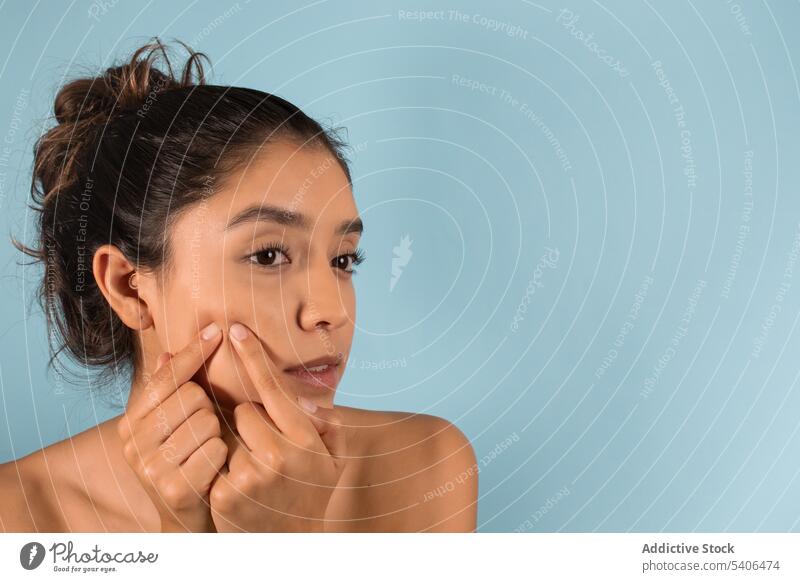 Junge Frau knallt Pickel auf Wangen auf blauem Hintergrund drücken Pop Hautpflege Schönheitsprogramm Gesichtsbehandlung Teint richtig Vorschein Porträt