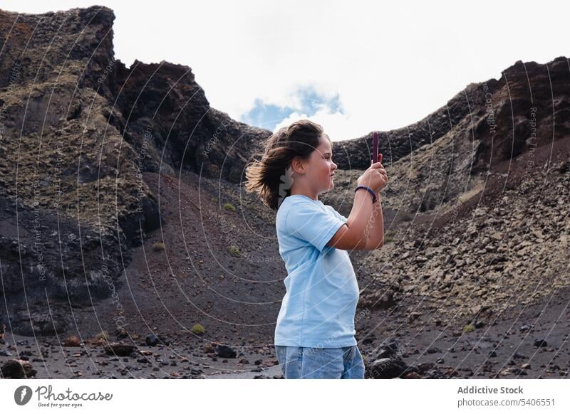 Lächelndes Kind, das in bergigem Gelände Fotos mit dem Smartphone macht Reisender benutzend fotografieren Vulkan erkunden Krater Landschaft Abenteuer Mädchen