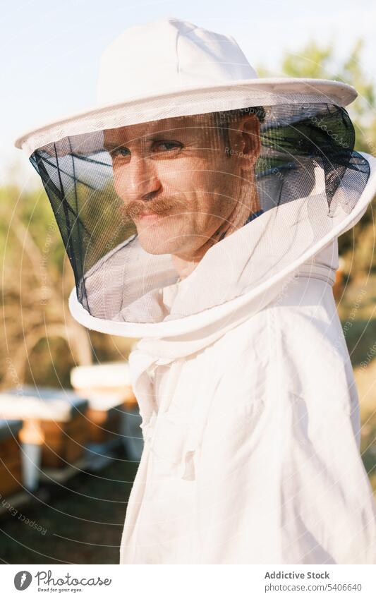 Männlicher Imker bei der Arbeit im Bienenstock an einem sonnigen Tag Mann Bienenkorb Feld Arbeitsbekleidung Uniform behüten Sommer Mundschutz Tracht männlich