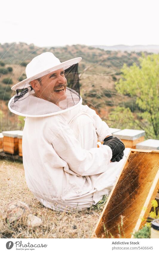 Glücklicher Imker mit einem Teil des Bienenstocks im Bienenhaus Bienenkorb heiter behüten Tracht Lächeln Wabe Mann männlich Uniform Job Natur professionell