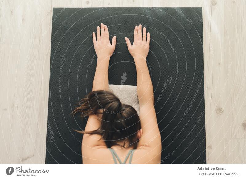 Unbekannte Frau übt Balasana-Pose auf Matte Sportlerin Kind-Pose Yoga üben Arme hochgezogen meditieren Asana Windstille Achtsamkeit heimwärts Vitalität Energie