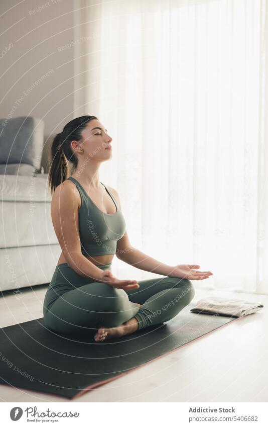 Frau meditiert in Padmasana-Pose zu Hause Sportlerin Lotus-Pose meditieren Yoga padmasana Asana heimwärts Achtsamkeit Windstille sich[Akk] entspannen üben